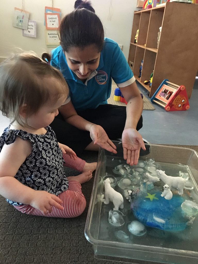 An educator and child exploring a melting ice sensory tray together. 
